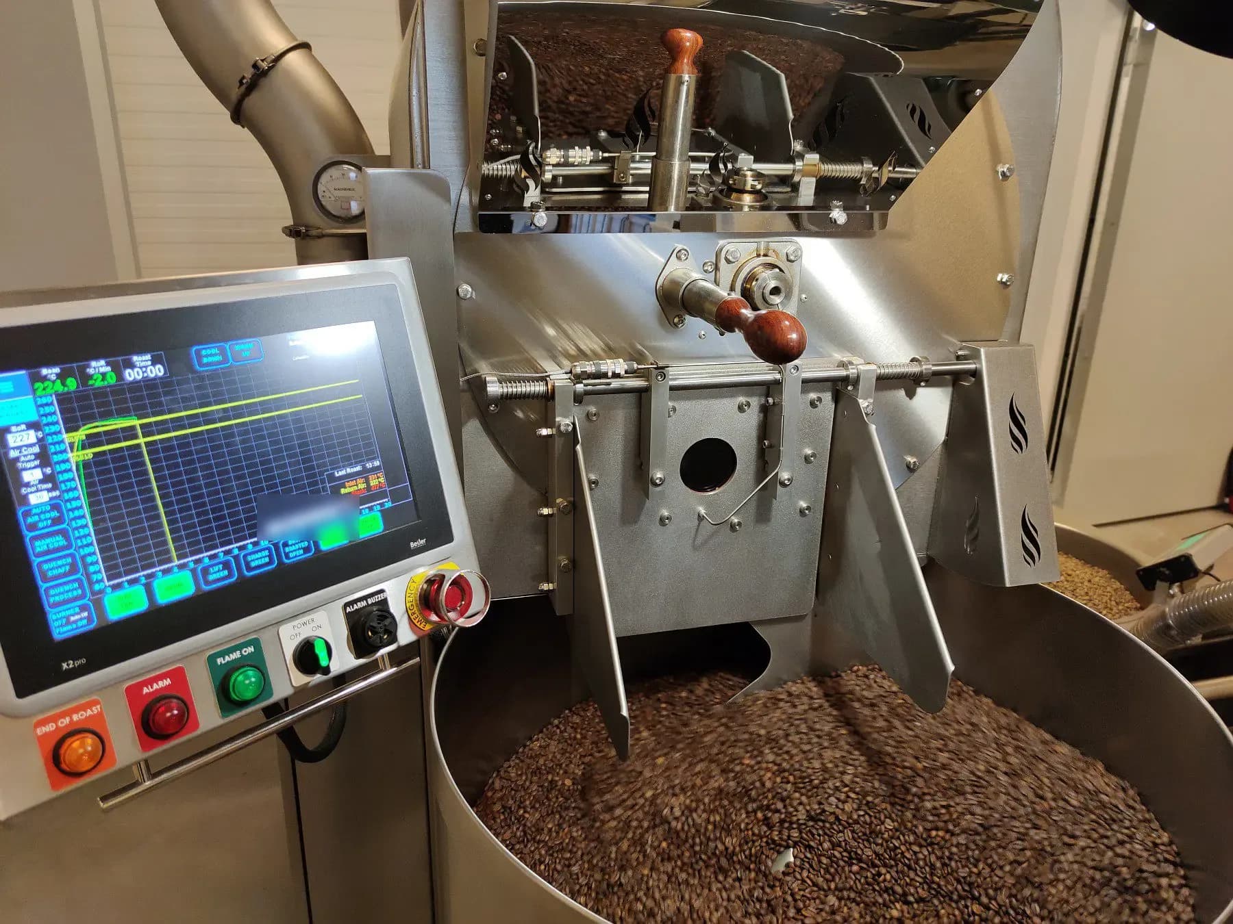 Kühlsieb unserer Rösterei voller frisch gerösteter Kaffeebohnen, dahinter das Bedienfeld mit Röstkurve